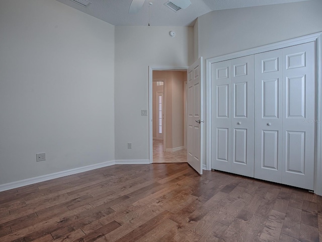 unfurnished bedroom with ceiling fan, wood-type flooring, a closet, and vaulted ceiling