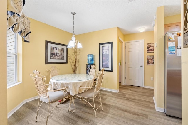 dining room with light wood-type flooring, a textured ceiling, and a chandelier