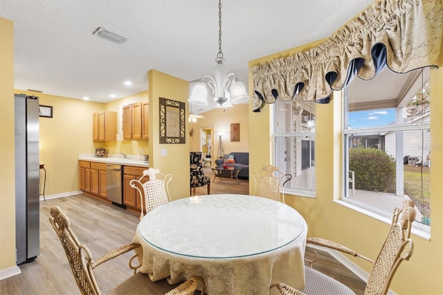 dining room with a textured ceiling, light hardwood / wood-style flooring, and a chandelier