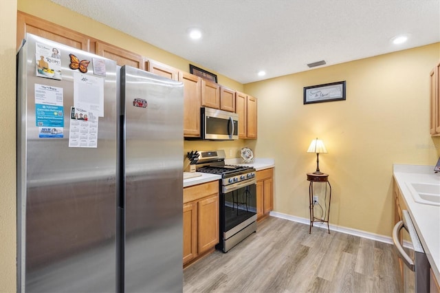 kitchen featuring light hardwood / wood-style floors, stainless steel appliances, and a textured ceiling