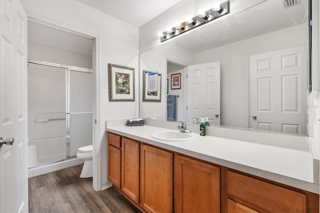 bathroom with toilet, a textured ceiling, walk in shower, wood-type flooring, and vanity