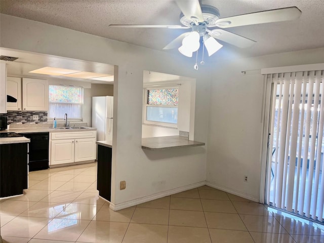 kitchen with light tile patterned floors, black dishwasher, freestanding refrigerator, light countertops, and backsplash