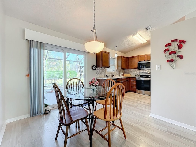 dining area featuring sink, a textured ceiling, light wood-type flooring, and vaulted ceiling