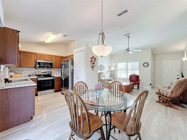 dining room with sink, a textured ceiling, lofted ceiling, ceiling fan, and light hardwood / wood-style flooring