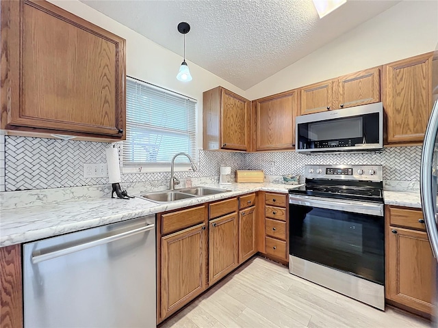 kitchen featuring vaulted ceiling, decorative light fixtures, light hardwood / wood-style floors, appliances with stainless steel finishes, and sink