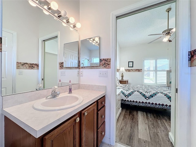 bathroom with a textured ceiling, ceiling fan, wood-type flooring, and vanity