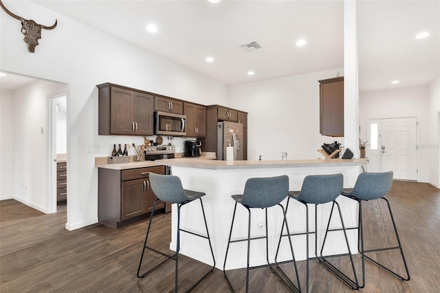 kitchen with dark wood-type flooring, a breakfast bar, stainless steel appliances, and dark brown cabinets