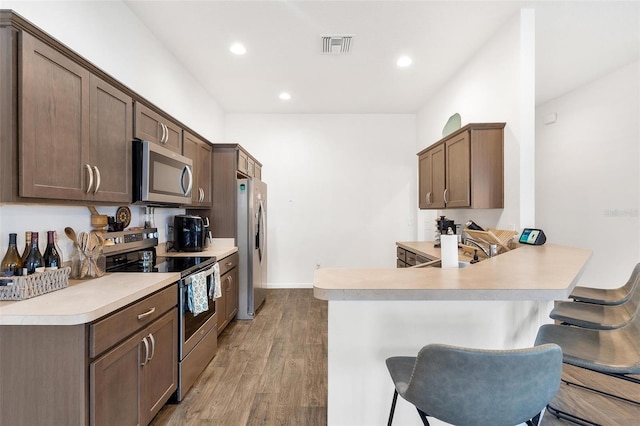 kitchen with light hardwood / wood-style floors, a breakfast bar, kitchen peninsula, sink, and appliances with stainless steel finishes