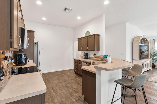 kitchen with dishwasher, kitchen peninsula, a kitchen bar, sink, and wood-type flooring