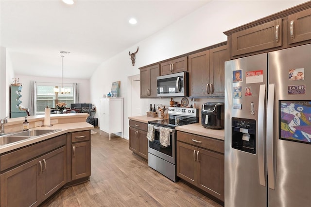 kitchen featuring lofted ceiling, light hardwood / wood-style floors, pendant lighting, an inviting chandelier, and appliances with stainless steel finishes