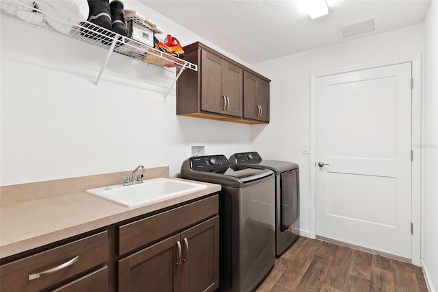 washroom featuring a textured ceiling, cabinets, dark wood-type flooring, washing machine and clothes dryer, and sink