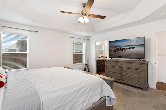 carpeted bedroom with ceiling fan, multiple windows, a tray ceiling, and ensuite bathroom