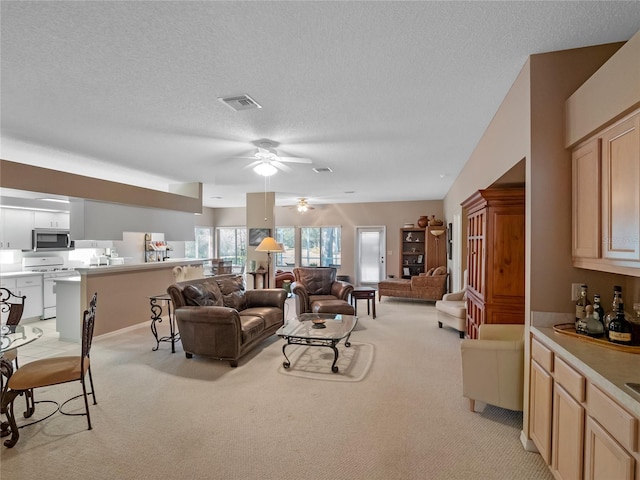 living room featuring ceiling fan, light colored carpet, and a textured ceiling