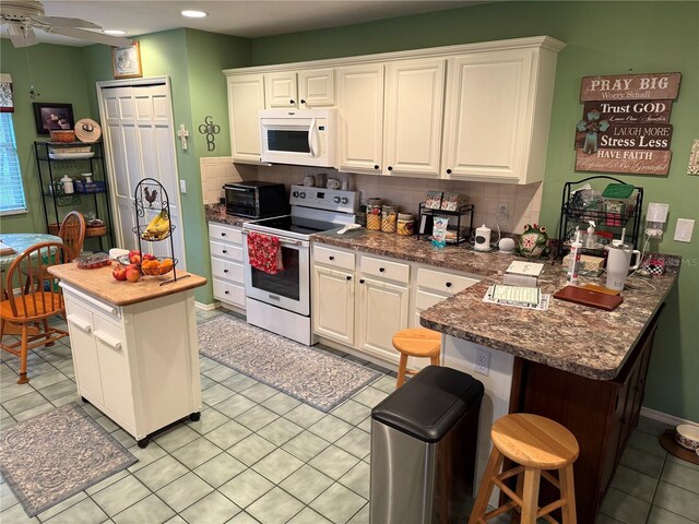 kitchen featuring white cabinets, a center island, white appliances, a kitchen breakfast bar, and decorative backsplash