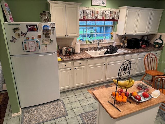 kitchen with white fridge, sink, white cabinetry, light tile patterned flooring, and tasteful backsplash