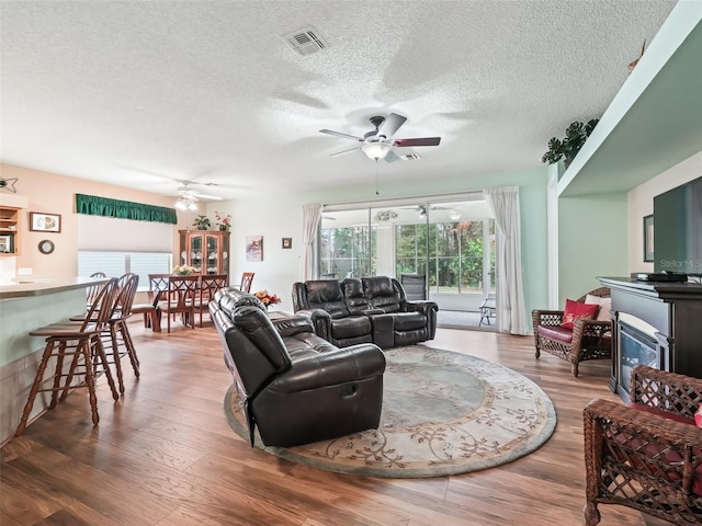 living room featuring ceiling fan, a textured ceiling, and wood-type flooring