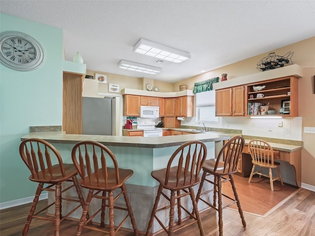 kitchen with kitchen peninsula, backsplash, white appliances, light hardwood / wood-style floors, and a breakfast bar area