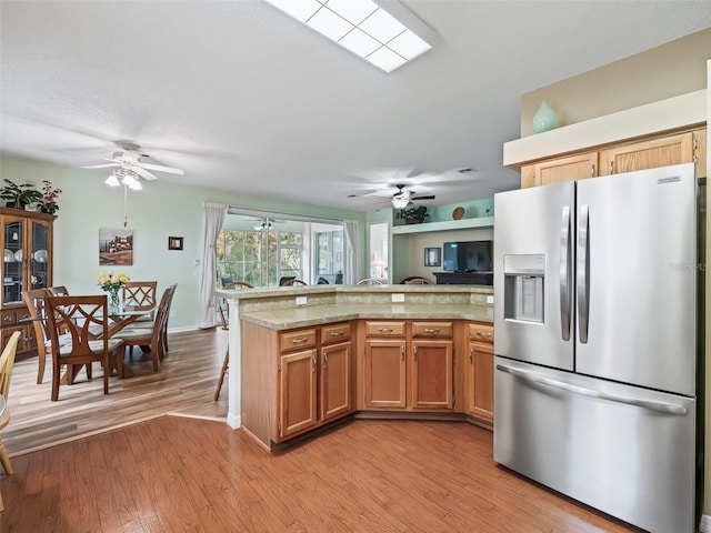 kitchen featuring light stone counters, stainless steel fridge, light hardwood / wood-style flooring, and ceiling fan