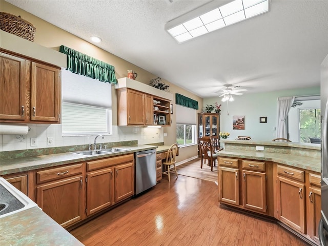 kitchen featuring stainless steel dishwasher, sink, light wood-type flooring, tasteful backsplash, and a textured ceiling