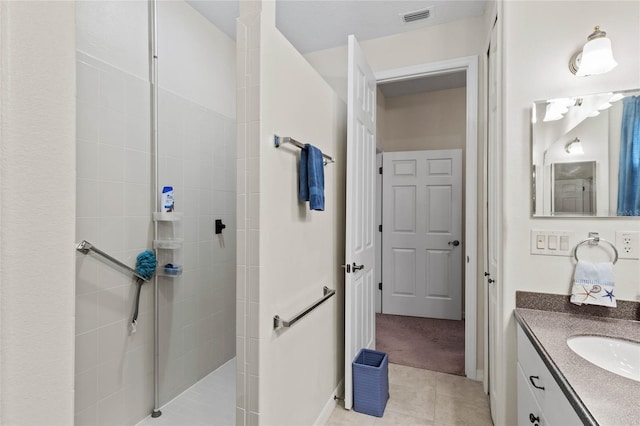 bathroom with tile patterned flooring, a tile shower, and vanity