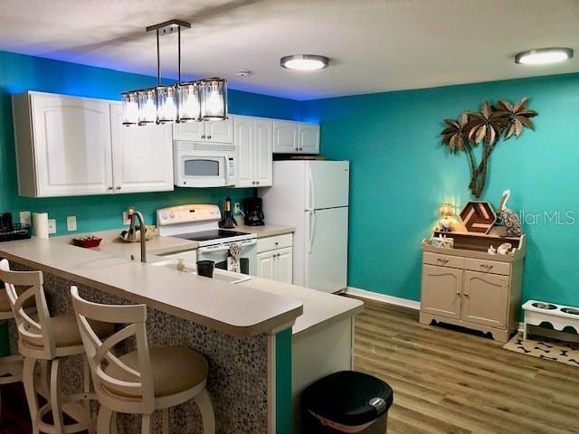 kitchen with white appliances, white cabinetry, hanging light fixtures, and kitchen peninsula