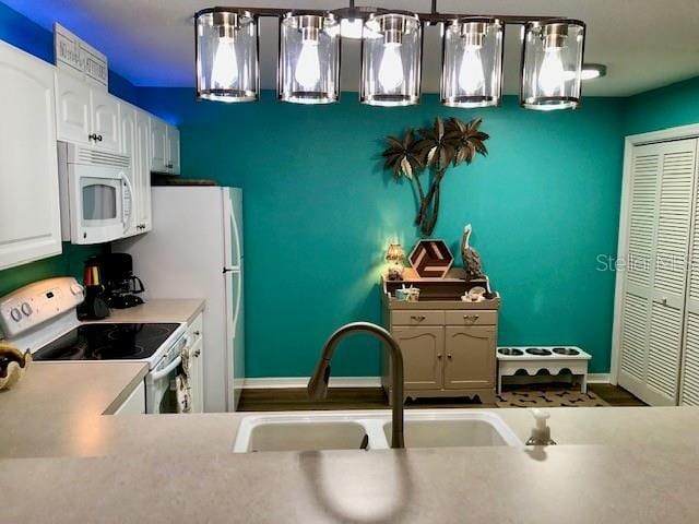 kitchen featuring sink, white appliances, hanging light fixtures, and white cabinets