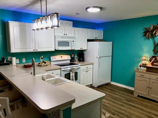 kitchen featuring white appliances, white cabinetry, hanging light fixtures, and kitchen peninsula