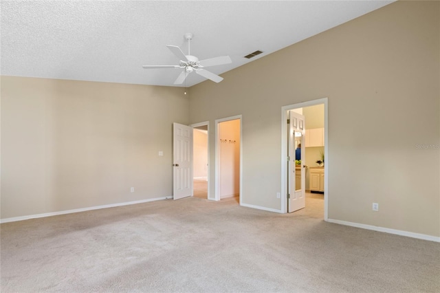 unfurnished bedroom with ensuite bathroom, a walk in closet, ceiling fan, and light carpet