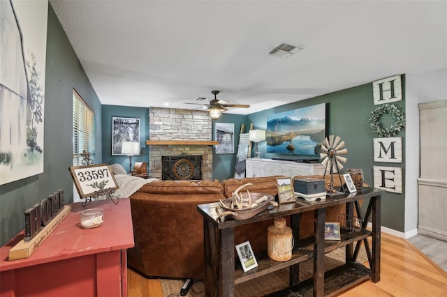 living room with light hardwood / wood-style floors, ceiling fan, and a stone fireplace