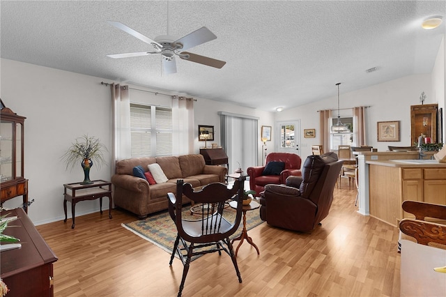 living room with ceiling fan, vaulted ceiling, light hardwood / wood-style flooring, and a textured ceiling