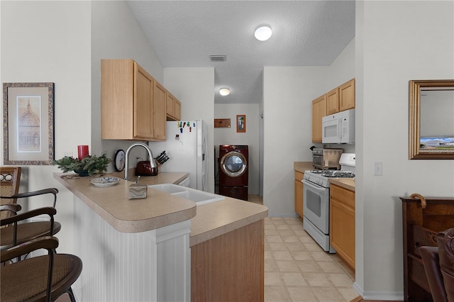 kitchen with white appliances, a kitchen bar, light brown cabinetry, washer / clothes dryer, and kitchen peninsula