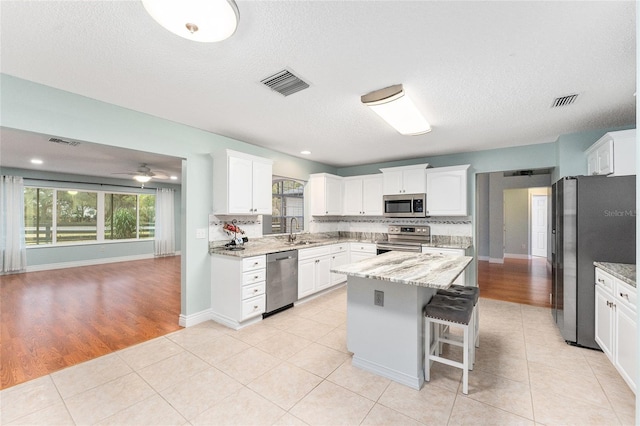 kitchen featuring appliances with stainless steel finishes, sink, white cabinets, light stone countertops, and a kitchen island