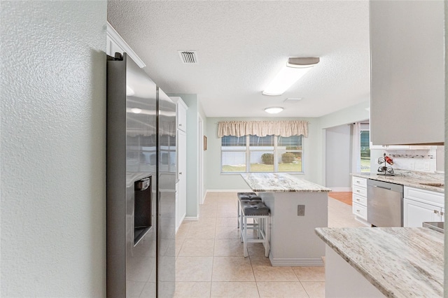 kitchen featuring light stone countertops, dishwasher, white cabinetry, a kitchen island, and a breakfast bar