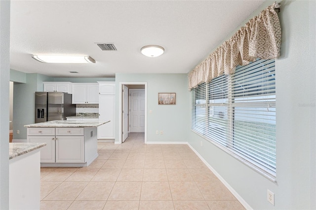 kitchen featuring stainless steel fridge, white cabinetry, light tile patterned floors, light stone counters, and a textured ceiling