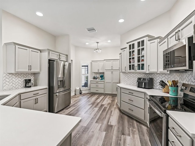 kitchen featuring light hardwood / wood-style floors, gray cabinets, stainless steel appliances, tasteful backsplash, and pendant lighting