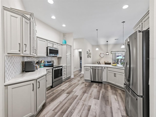 kitchen with tasteful backsplash, kitchen peninsula, hanging light fixtures, light wood-type flooring, and appliances with stainless steel finishes