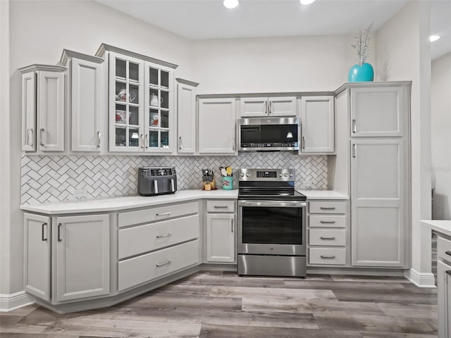 kitchen featuring hardwood / wood-style flooring, gray cabinetry, stainless steel appliances, and tasteful backsplash