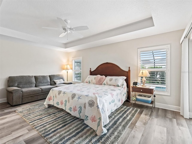 bedroom featuring ceiling fan, a closet, wood-type flooring, and a tray ceiling