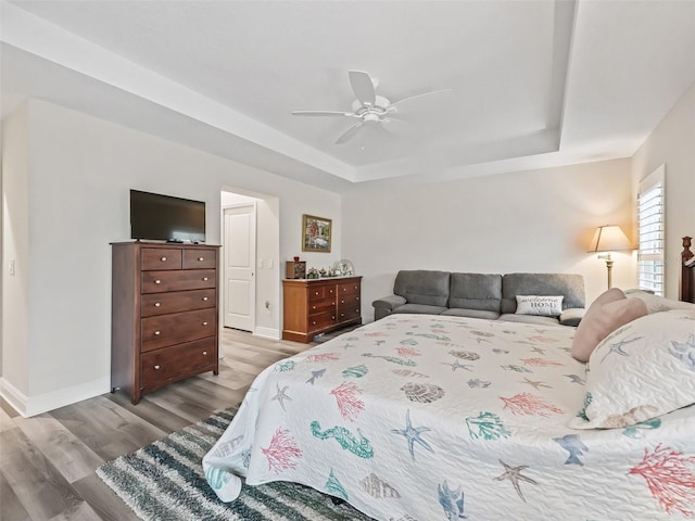 bedroom with a raised ceiling, ceiling fan, and light hardwood / wood-style floors