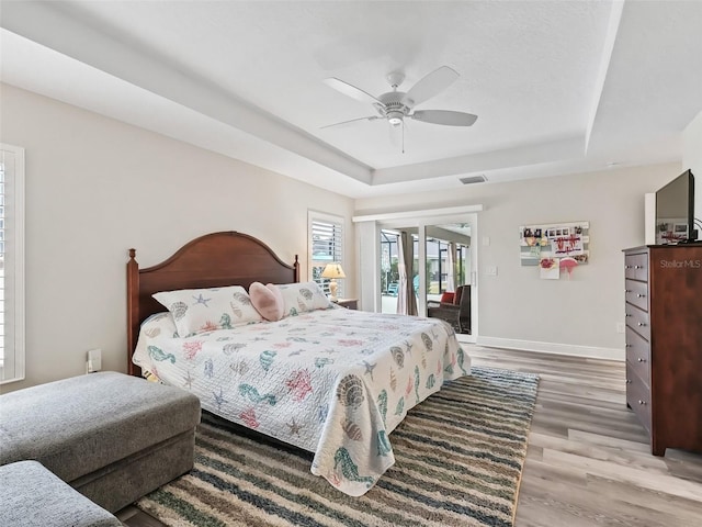 bedroom featuring ceiling fan, light hardwood / wood-style floors, a raised ceiling, and access to outside