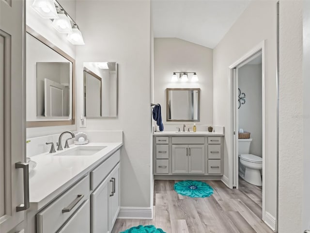 bathroom with hardwood / wood-style floors, toilet, vanity, and vaulted ceiling