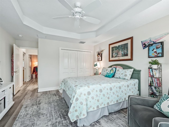 bedroom with a raised ceiling, a closet, dark wood-type flooring, and ceiling fan