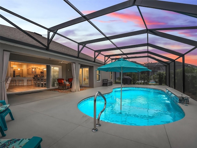 pool at dusk with ceiling fan, a lanai, pool water feature, and a patio