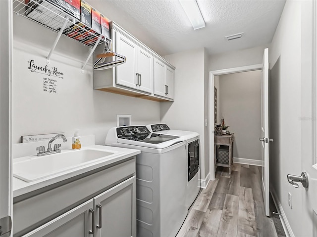 washroom featuring washer and dryer, light hardwood / wood-style floors, sink, a textured ceiling, and cabinets