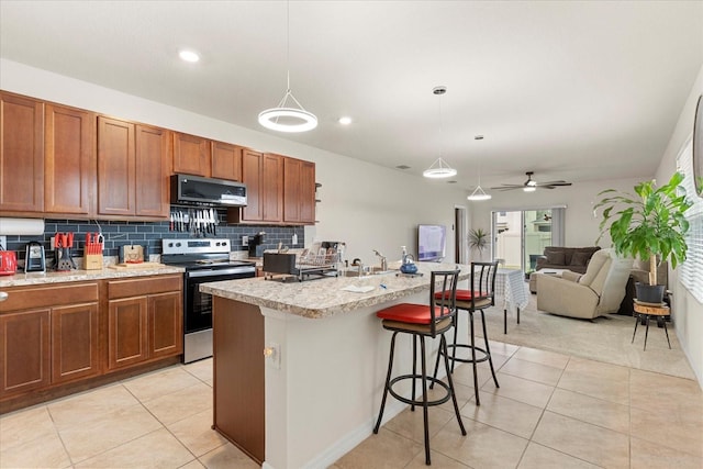 kitchen featuring decorative light fixtures, ceiling fan, an island with sink, a breakfast bar, and appliances with stainless steel finishes