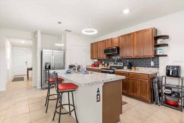 kitchen with pendant lighting, stainless steel appliances, light tile patterned floors, a kitchen island with sink, and sink