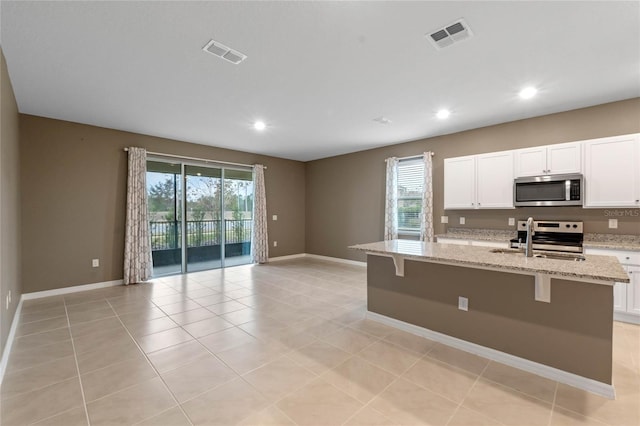 kitchen featuring light stone counters, white cabinetry, stainless steel appliances, and an island with sink