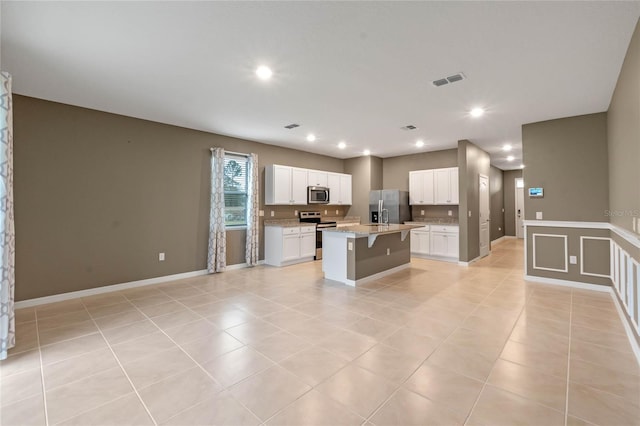 kitchen featuring light tile patterned floors, a kitchen island with sink, appliances with stainless steel finishes, and a breakfast bar area