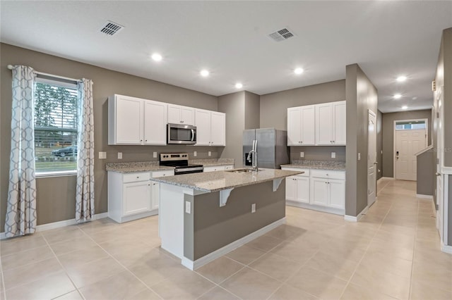 kitchen with light stone counters, white cabinetry, stainless steel appliances, and an island with sink