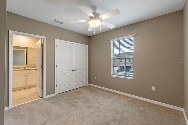 unfurnished bedroom featuring ceiling fan, ensuite bath, a textured ceiling, light carpet, and a closet